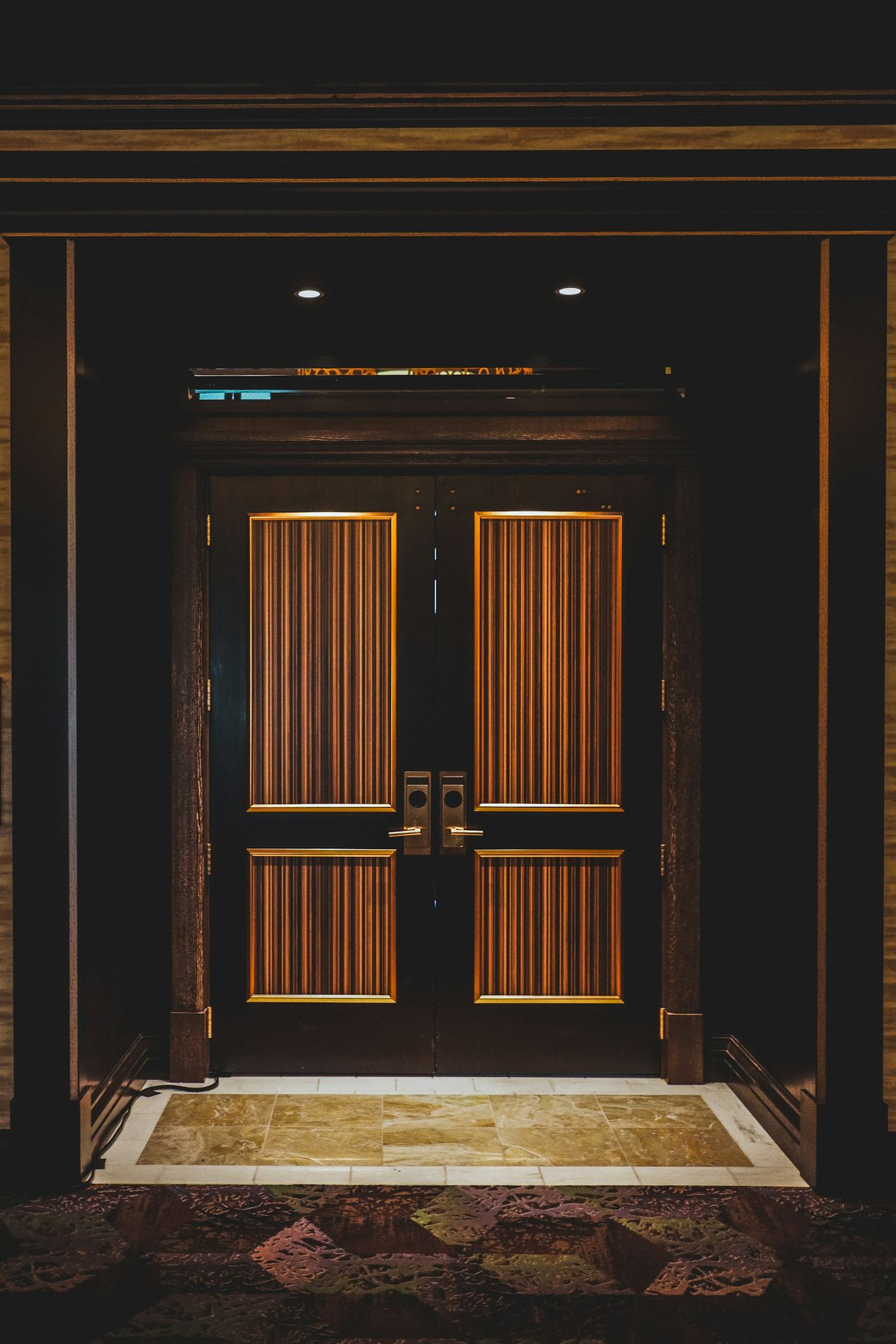 An elegant pair of dark wooden doors framed with brass detail and warm overhead lighting