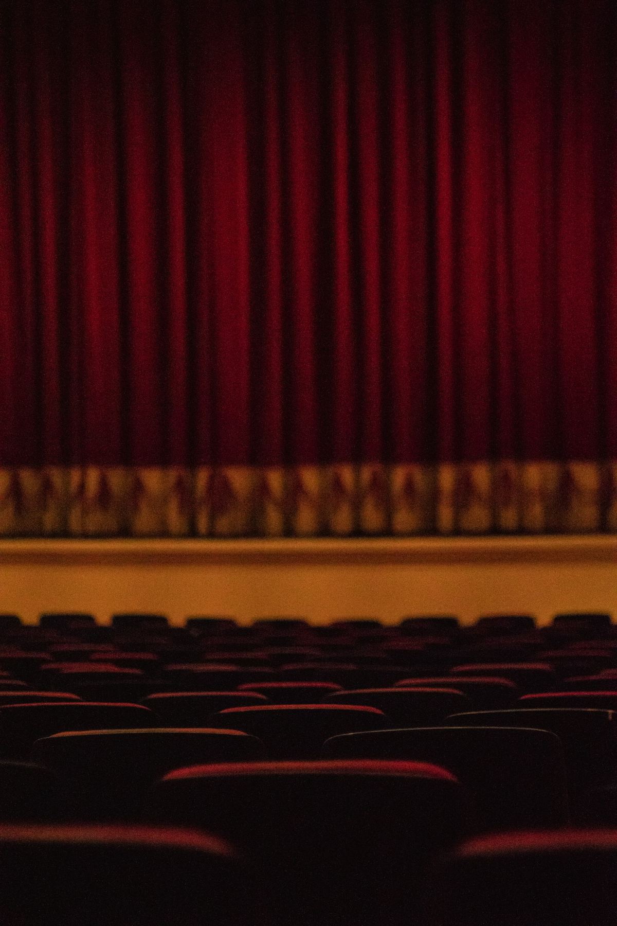 An empty theater interior with a deep red curtain and rows of seats
